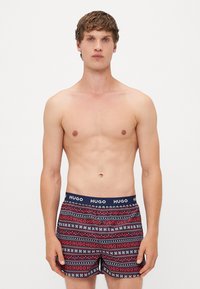 Boxeri navy cu dungi modelate roșii și albe, având un tiv de marcă cu logo-ul "HUGO". Materialul pare a fi neted și elastic.