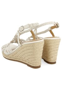 Sandalias de cuña blancas tejidas con correas trenzadas, hebilla ajustable y un talón de yute texturizado. Diseñadas de manera sostenible para brindar comodidad y estilo.