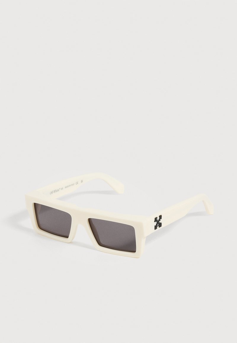 Lunettes de soleil rectangulaires blanches avec des verres foncés et un logo noir sur la branche, présentées sur un fond blanc uni.