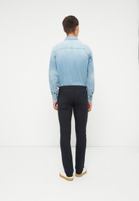 Lyseblå denimskjorte med falmet bakstykke, kombinert med tettsittende svarte bukser. Modellen har på seg hvite sko med lysebrun såle.