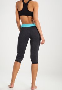 Haut court de sport noir avec design dos nageur, associé à un legging capri gris charbon avec une taille turquoise et une texture lisse.