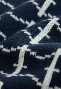 Marineblauwe gebreide stof met een wit geometrisch patroon. De textuur is zacht en licht pluizig, met verhoogde steken die diepte creëren.