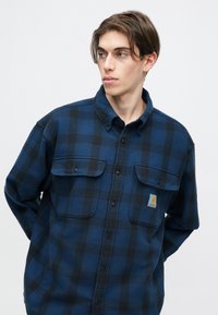 Μπλε και μαύρο πουκαμίσα καρό από φλις με κολάρο που κλείνει με κουμπιά, δύο τσέπες στο στήθος και μια μικρή επικάλυψη λογότυπου στην αριστερή τσέπη.