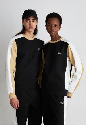 Felpe color block nere e beige con dettagli bianchi, impreziosite dal logo Lacoste. Realizzate in un tessuto morbido e abbinate a pantaloni coordinati.