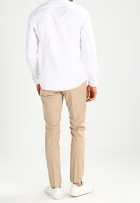 Vit skjorta med långa ärmar och knappdetaljer, matchad med beiga byxor och vita sneakers; mjukt tyg med en skräddarsydd passform.