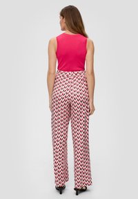 Roze mouwloze top gecombineerd met witte broek met een rood en zwart hartpatroon. Losse pasvorm met een elastische tailleband en zwarte schoenen.