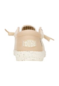 Beige Sneaker mit einem Obermaterial aus Stoff. Merkmale sind eine abgerundete Form, eine cremefarbene gesprenkelte Sohle und das "HEY DUDE"-Logo auf der Rückseite.