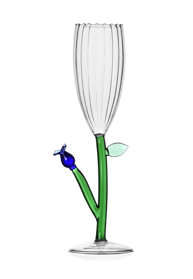 Przezroczysta szklanka w kształcie fletu z pionowymi żebrowaniami, zielona noga przypominająca łodygę kwiatu, niebieski kwiat jako akcent oraz zielony detal w postaci liścia.