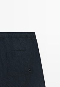 Short bleu marine texturé avec une ceinture élastique et une poche arrière dotée d'un petit œillet en métal.