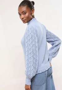 Hele sinine kudumista sweater kõrge kraega ja tekstuursete, pitsiliste puffvarrukatega; sisaldab soonitud mansette ja äärist.