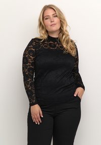 Svart spetsblus med lång ärm som har blommönster och en slät kropp. Matchad med åtsittande svarta byxor som framhäver textur och design.