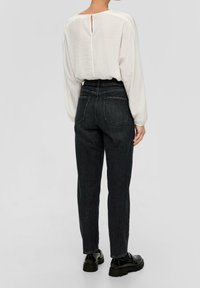 Blusa bianca a maniche lunghe con dettaglio a occhiello sulla schiena, abbinata a jeans neri in denim a vita alta, con gamba affusolata e due tasche posteriori.