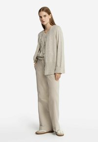 Ljusbeige cardigan med ribbade ärmar, bärs över en texturerad tröja och kombineras med löst sittande ljusbeiga byxor och avslappnade skor.