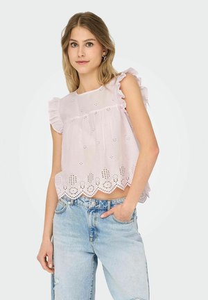 Jasnoróżowa bawełniana bluzka z falbaniastymi rękawami, haftowanymi detalami w kształcie oczek oraz falbaniastym dołem. Sparowana z dżinsami z wysokim stanem.