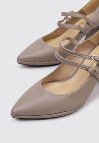 Chaussures beiges à bout pointu avec deux brides réglables, en cuir lisse, semelle intérieure rembourrée et design de semelle fine.