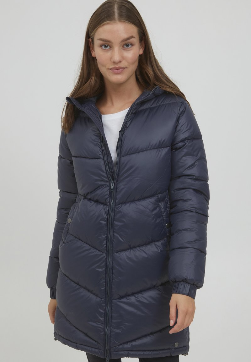 Marinblå pufferjacka med huva, quiltad design, dragkedjestängning och elastiska muddar. Tillverkad av glänsande, lätt material.
