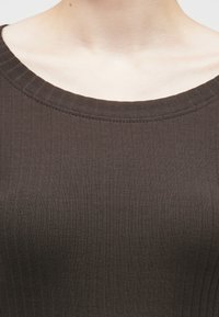 Σκούρο καφέ ριβέ μπλουζάκι με φαρδύ, στρογγυλεμένο λαιμό και διακριτή υφή. Το ύφασμα είναι απαλό, με κατακόρυφες γραμμές και εφαρμοστή σιλουέτα.