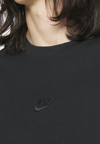 Černé bavlněné tričko s kulatým výstřihem, na prsou malé černé vyšívané logo Nike. Hladká textura, jednoduchý design, minimalistický styl.