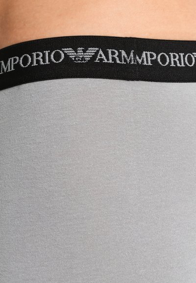 Material gri cu o textură netedă, având un brâu elastic negru inscripționat cu "ARMANI" în litere argintii și un logo cu o vultur.