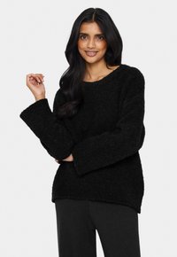 Crni preveliki pulover od teksturirane, mekanne tkanine; rebrasti rukavi i širok izrez, uparen sa sivim hlačama.