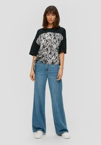 Czarny i biały t-shirt w wzór paisley, oversized, z krótkimi rękawami, zestawiony z szerokimi niebieskimi dżinsami i białymi trampkami.