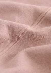 Blødt pink bomuldsstof med en glat overflade og let stræk, der har et diskret vævet mønster og rene syninger langs kanterne.