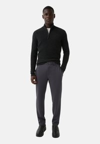 Donkergrijze sweater met ritssluiting en geribbelde textuur, gecombineerd met lichtgrijze broek en zwarte enkellaarzen. Eenvoudig en gestroomlijnd ontwerp.