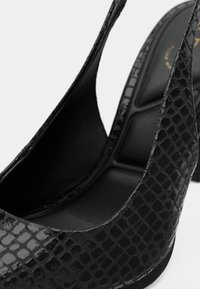 Svarte slingbacks med høye hæler, blankt teksturert mønster som likner slangeskinn, og polstrede innersåler.