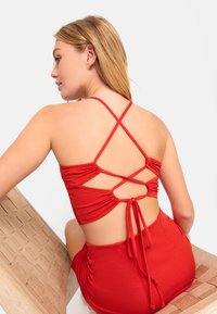 Completo due pezzi rosso con top aderente caratterizzato da spalline incrociate e un laccio posteriore, abbinato a un pantalone a vita alta coordinato.