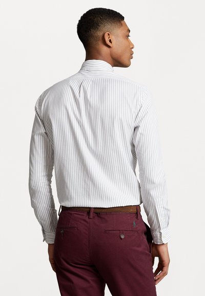 Cămașă albă cu dungi gri; cusături vizibile; asortată cu pantaloni burgundy ce au două buzunare la spate și o curea maro.