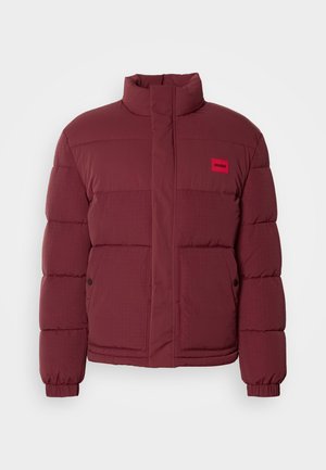 Giacca a puffo bordeaux con colletto alto, texture trapuntata e patch rosso del marchio. Caratterizzata da chiusura a scatto e tasche laterali.