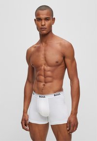 Weiße Herren-Boxershorts mit einem schwarzen Elastikbund, der mit "BOSS"-Branding versehen ist. Glatte Textur, körperbetontes Design und Länge bis zur Mitte des Oberschenkels.