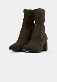 Bottines en daim marron avec un design lâche, bout pointu et un talon épais. Texture lisse avec un minimum de détails de couture.