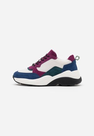 Masywne sneakersy z białą siateczkową cholewką, fioletowymi i zielonymi zamszowymi nakładkami, niebieskim zamszowym noskiem i piętą, czarnymi sznurowadłami oraz grubą białą i czarną podeszwą.