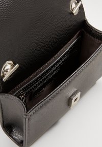 Piccola borsa a mano in pelle nera texturizzata con patta aperta, tasca interna con zip e chiusura rettangolare in tonalità argento sul davanti.