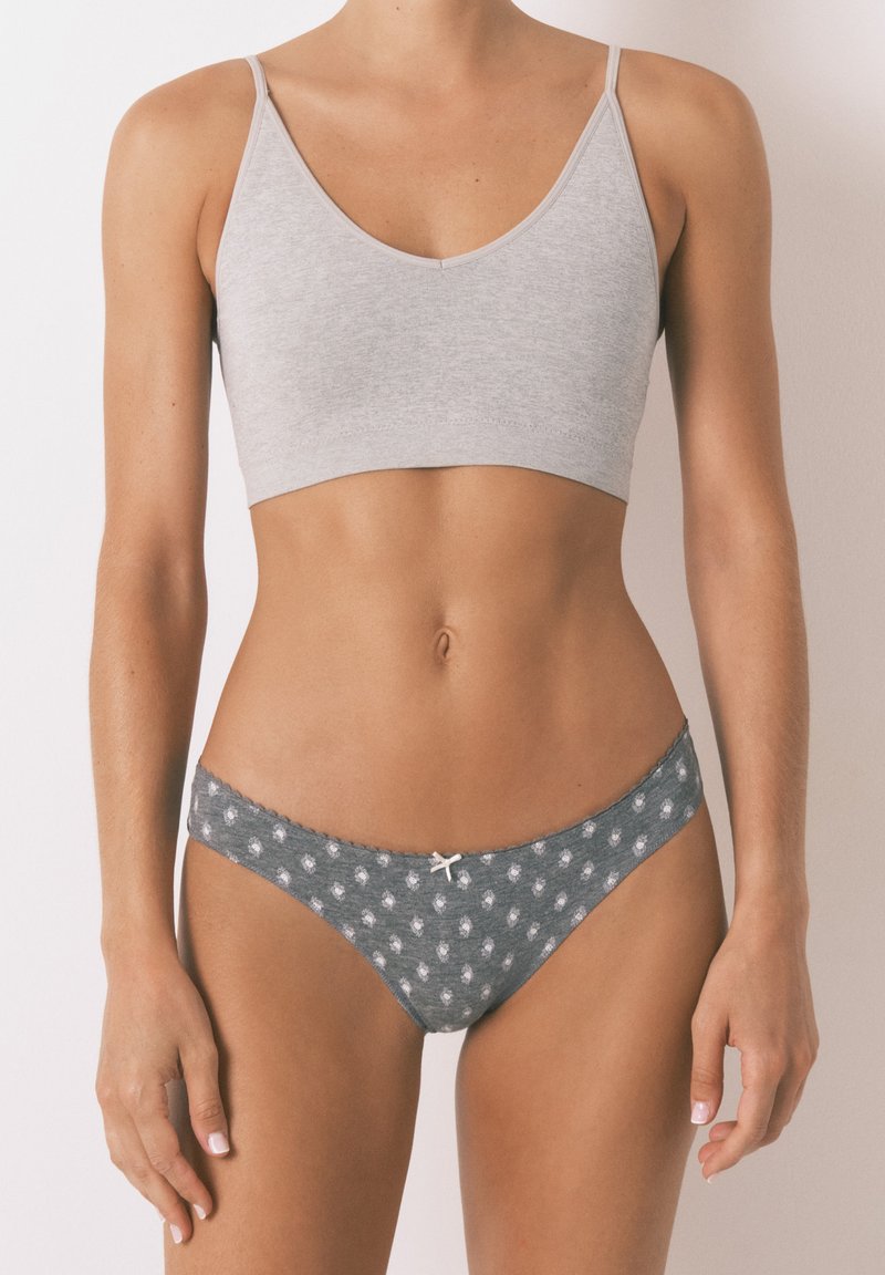 Grijze katoenen bralette met dunne bandjes, gecombineerd met grijze slip met een patroon van kleine witte stippen en een witte strikaccent.