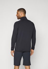 Donkergrijze sporttop met lange mouwen en hoge kraag, van gestructureerde stof met contrasterende stiksels, gecombineerd met donkere shorts.