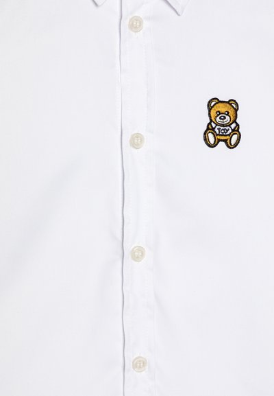 Camicia bianca con bottoni, realizzata in cotone con una finitura testurizzata, caratterizzata da un logo ricamato di un orsetto in oro e nero sul petto.