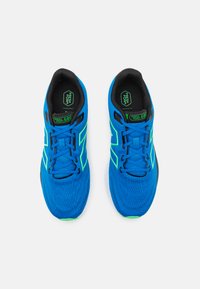 Blauwe sportieve sneakers met groene accenten, mesh bovenmateriaal, textuur en zwarte binnenkant. Veters en branding op de tong zichtbaar.