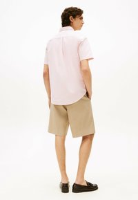 Jasnoróżowa koszula na krótki rękaw z guzikami, z detalem na plecach, zestawiona z beżowymi szortami w prążki i czarnymi loafersami.