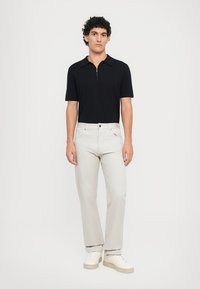 Zwarte polo met korte mouwen en ritssluiting, gecombineerd met lichtgrijze rechte broek en witte sneakers.