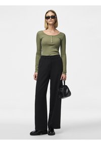 Grön ribbad långärmad topp med knapptyg, tillsammans med svarta vida byxor. Svart handväska och solglasögon fulländar outfiten.