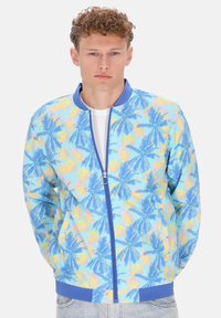 Giubbotto bomber leggero con sfondo blu e stampe colorate di foglie di palma, chiusura frontale con zip e polsini e orlo a coste di colore blu uniforme.