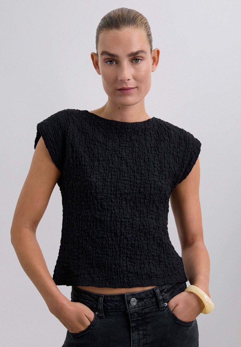 Top corto a maniche corte nero con scollo rotondo. Caratterizzato da un tessuto stropicciato e una vestibilità comoda, abbinato a un denim scuro.