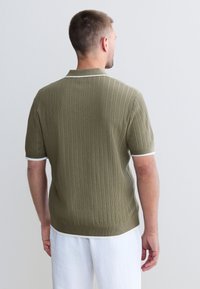 Tricou polo verde măsliniu cu mânecă scurtă și textură reiată, cu guler și accente albe pe mâneci, design mulat, afișat din spate.