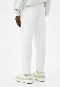 Jeans blancos ajustados de mezclilla, con dos bolsillos traseros de parche. Combinados con zapatillas beige y blancas, que muestran una textura suave.