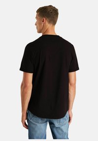 Schwarzes T-Shirt mit kurzen Ärmeln, rundem Halsausschnitt und abgerundetem Saum. Hergestellt aus weichem Stoff mit dezenten Nähten auf der Rückseite.