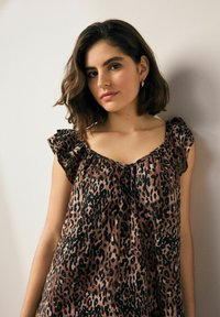 Halenka s leopardím vzorem v hnědé a černé barvě, s volnými rukávy, uvolněným střihem a detailem na zavazování u výstřihu. Hladká textilie.