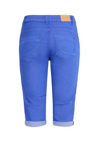 Jean bleu court avec revers retroussés, deux poches arrière avec rivets, passants pour ceinture et un patch de marque en cuir fauve sur la ceinture.