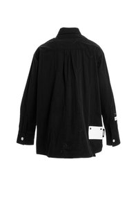 Camisa negra con patrones circulares bordados, cuello puntiagudo, mangas largas y un bolsillo de parche blanco en el lado izquierdo.